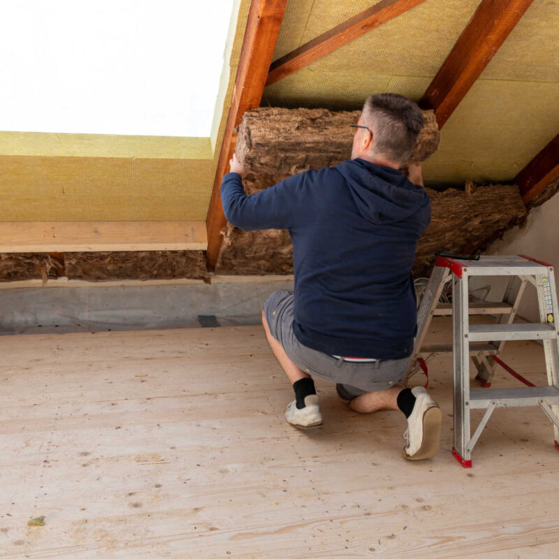 Handwerker verlegt Dämm-Material auf dem Dachboden