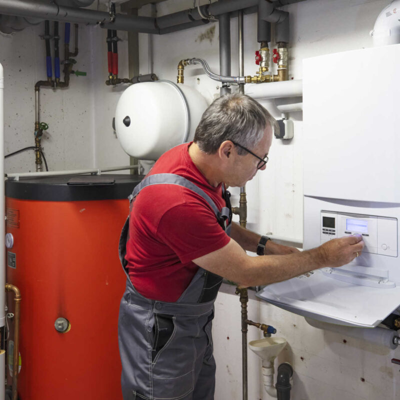 Heizungsmonteur überprüft die Heizungsanlage im Keller eines Wohnhauses.